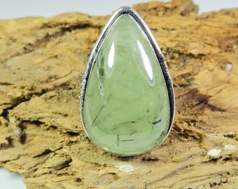 Könnte beinhalten: Ein tropfenförmiger Ring mit einem grünen Aventurin-Edelstein, der in einer silbernen Fassung gefasst ist. Der Stein hat eine durchscheinende grüne Farbe mit schwarzen Einschlüssen.