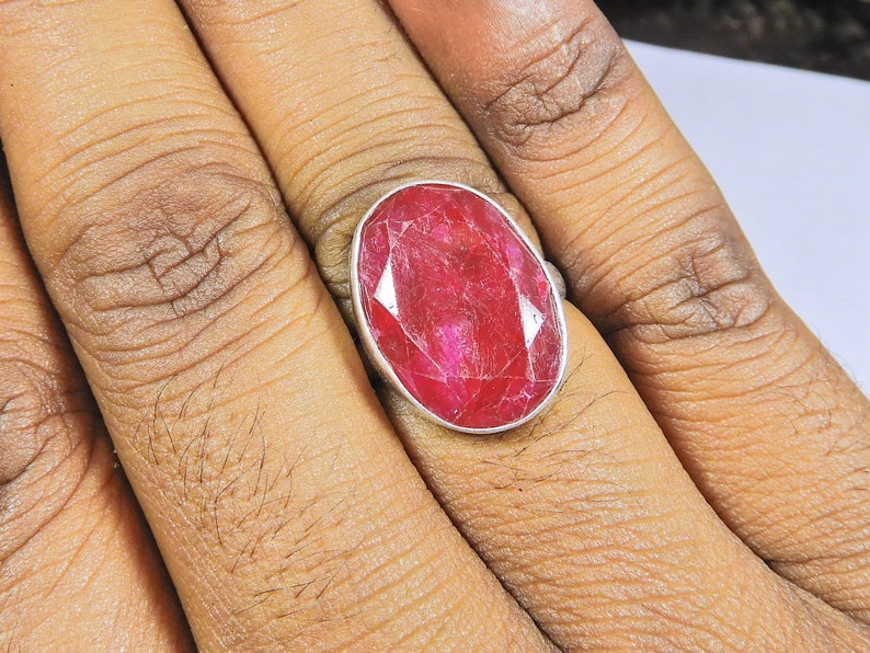 May include: A silver ring featuring a large, oval-shaped, red ruby gemstone.