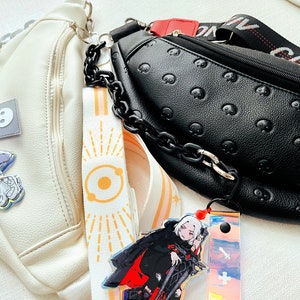 Könnte beinhalten: Eine weiße Bauchtasche mit weißer Kette und Anime-Figur-Anhänger neben einer schwarzen Bauchtasche mit Totenkopf-Prägung, schwarzer Kette, einem Riemen mit der Aufschrift CONVERSE und einem Anime-Figur-Anhänger mit einem Schwert-Symbol.