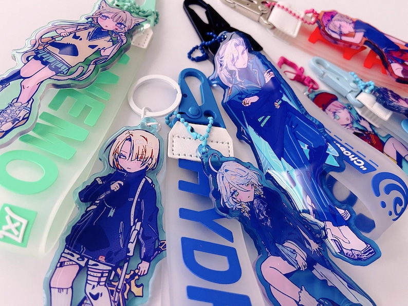 May include: Collection of anime-style acrylic keychains featuring colorful illustrations of characters. The keychains have various designs, including characters with cat ears and long hair. Some keychains have text in English and Japanese.