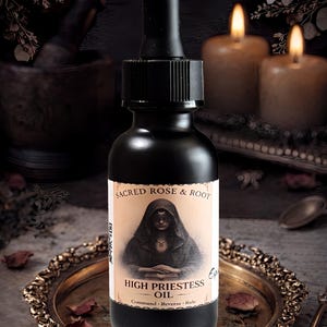 Puede incluir: Una botella negra de "High Priestess Oil" con una etiqueta que presenta una ilustración de una figura encapuchada. La botella está sobre una bandeja decorativa dorada con pétalos de rosa secos. El texto "Sacred Rose & Root" está encima de la etiqueta.