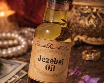 Könnte beinhalten: Kleine Glasflasche gefüllt mit goldenem Öl, beschriftet mit "Jezebel Oil". Das Etikett ist im Vintage-Stil mit dem Text "Sacred Rose & Root". Die Flasche hat einen schwarzen Deckel. Der Hintergrund umfasst Perlen, Geld und lila Blumen.