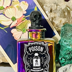 Può includere: Una piccola bottiglia di vetro iridescente con un tappo a forma di teschio nero. La bottiglia ha un'etichetta in bianco e nero che recita "Poison Deadly Nightshade".