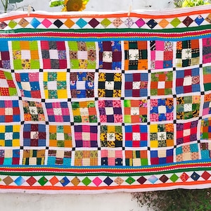 May include: A colorful patchwork quilt with a geometric pattern. The quilt is made of squares of different fabrics, each with a unique design. The quilt is bordered by a colorful trim.