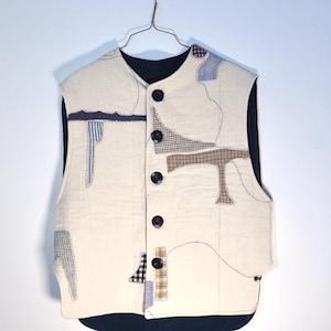 May include: A white quilted vest with a navy blue lining and patchwork details. The vest has a button closure and a stand-up collar.