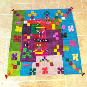 May include: A colorful patchwork quilt with a geometric design. The quilt is made up of squares of different colors and patterns, including green, blue, red, yellow, purple, and pink. The quilt is edged with a fringe.