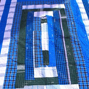 May include: A patchwork quilt with a geometric design in shades of blue, white, and green. The quilt is made of different fabrics, some with a plaid pattern.