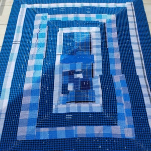 Könnte beinhalten: Eine blaue und weiße karierte Steppdecke mit einem konzentrischen quadratischen Muster. Die Steppdecke besteht aus verschiedenen Blautönen und hat einen weißen Rand.