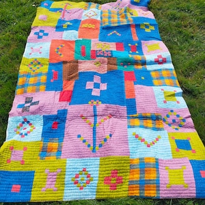 Puede incluir: Una colcha de retazos colorida con una variedad de patrones geométricos en tonos de azul, verde, rosa, naranja y amarillo. La colcha está hecha de cuadrados y rectángulos, y los patrones se crean uniendo diferentes telas.