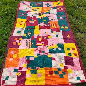 Puede incluir: Una colcha de retazos colorida con cuadrados de rosa, amarillo, naranja, rojo, verde y blanco. La colcha está hecha de tela de algodón y tiene un diseño cosido a mano.