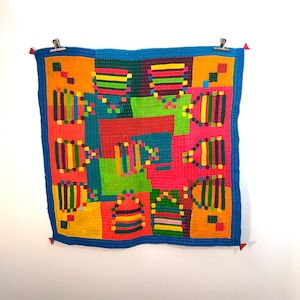 Puede incluir: Una colcha de retazos colorida con un diseño geométrico. La colcha está hecha de varias telas en tonos de rojo, naranja, amarillo, verde, azul y morado. La colcha está cosida con un hilo contrastante.