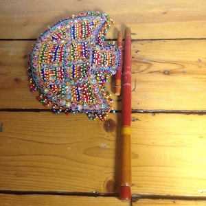 Può includere: Un ventaglio di perline colorate con un manico di legno. Il ventaglio è decorato con perline in tonalità di rosso, blu, verde, giallo e bianco. Il manico è rosso con una striscia gialla.