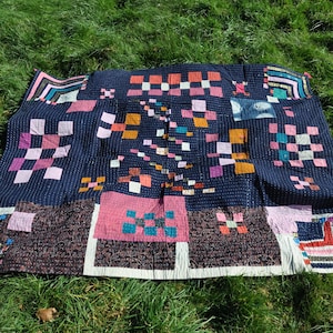 May include: A patchwork quilt with a dark blue background and a variety of pink, orange, and teal squares. The quilt is made of different fabrics and textures, creating a unique and interesting design.