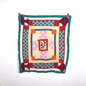 Peut inclure: Une tapisserie murale en crochet colorée avec un motif géométrique dans des tons de rouge, vert, bleu, rose et blanc.