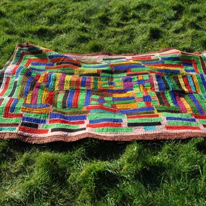 Puede incluir: Una colcha de retazos colorida con un patrón geométrico en tonos de rojo, verde, azul, amarillo y negro. La colcha está hecha de diferentes telas cosidas juntas para crear un diseño único.