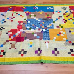 Op de afbeelding: Een kleurrijk patchwork-deken met een verscheidenheid aan vierkanten en rechthoeken in verschillende kleuren en patronen. Het deken is gemaakt van verschillende stoffen, waaronder katoen, zijde en wol. Het deken is een uniek en prachtig kunstwerk.