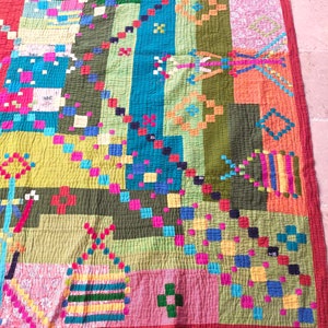 May include: A colorful patchwork quilt with a geometric pattern. The quilt is made of various fabrics in shades of green, blue, red, yellow, pink, and orange. The quilt is stitched together with a contrasting thread.