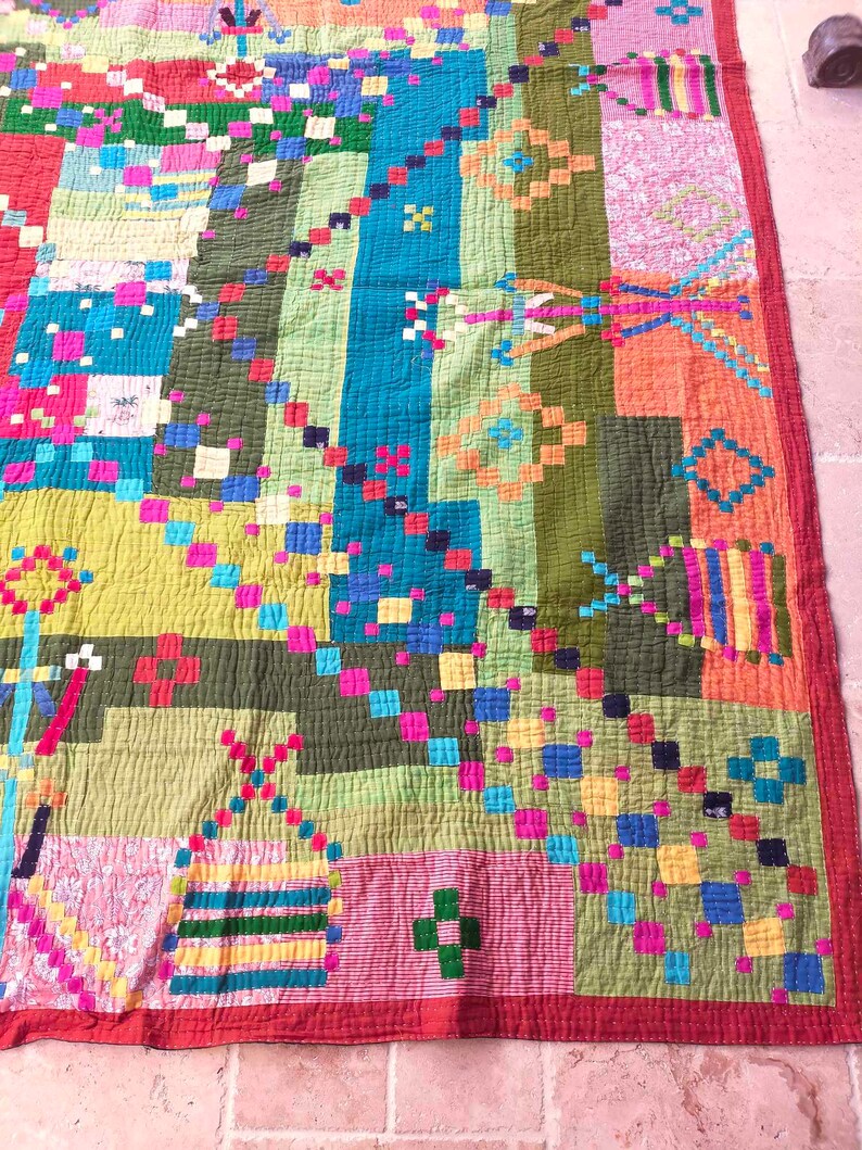 May include: A colorful patchwork quilt with a geometric pattern. The quilt is made of various fabrics in shades of green, blue, red, yellow, pink, and orange. The quilt is stitched together with a contrasting thread.