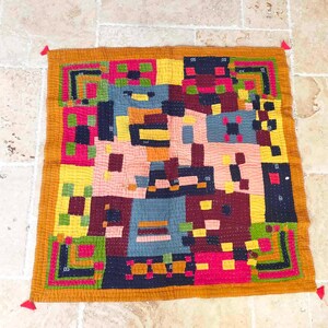 May include: A colorful patchwork quilt with a geometric design. The quilt is made of various fabrics in shades of red, yellow, blue, green, and brown. The quilt is edged with a gold fabric and has red tassels at each corner.