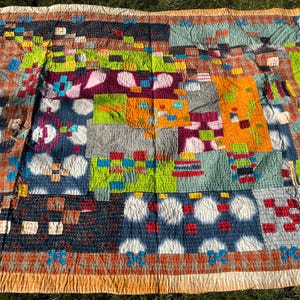 May include: A colorful patchwork quilt with a variety of patterns and colors. The quilt features squares of blue, orange, green, and purple fabric. The edges are trimmed with an orange border.