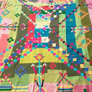May include: A colorful patchwork quilt with a geometric design. The quilt is made of various fabrics in shades of green, red, blue, yellow, and pink. The quilt is quilted with a simple stitch pattern.