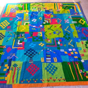 Op de afbeelding: Een kleurrijk patchwork-deken met geometrische patronen in tinten blauw, groen, geel, rood en oranje.