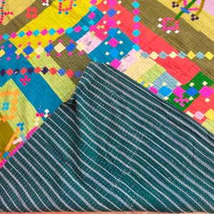 May include: A colorful patchwork quilt with a geometric pattern. The quilt is made of different fabrics in shades of green, blue, yellow, pink, and orange. The quilt is folded in half, revealing a dark green striped fabric on the underside.