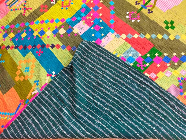 May include: A colorful patchwork quilt with a geometric pattern. The quilt is made of different fabrics in shades of green, blue, yellow, pink, and orange. The quilt is folded in half, revealing a dark green striped fabric on the underside.