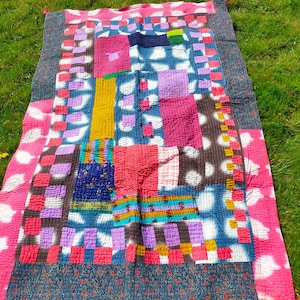 Puede incluir: Una colcha de retazos colorida con una variedad de telas y patrones, incluyendo rosa, morado, azul y blanco. La colcha está hecha de cuadrados y rectángulos, y tiene un borde con flecos.