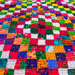Puede incluir: Una colcha de retazos colorida con una variedad de patrones florales y colores brillantes. La colcha está hecha de pequeños cuadrados cosidos juntos para crear un diseño más grande. La colcha es una obra de arte textil vibrante y alegre.