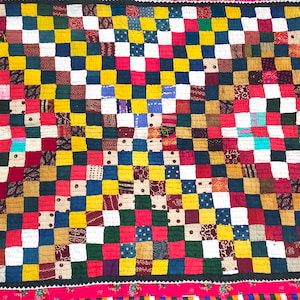 May include: A colorful patchwork quilt with a checkered pattern. The quilt is made of various fabrics in shades of red, yellow, blue, green, and white. The quilt is stitched together with a decorative stitch.