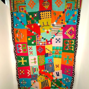 Puede incluir: Una colcha de retazos colorida con una variedad de patrones y diseños geométricos. La colcha está hecha de muchos colores diferentes, incluyendo rojo, naranja, amarillo, verde, azul y morado. La colcha está colgada en una pared.