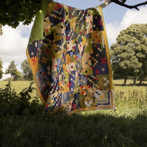 May include: A colorful patchwork quilt with geometric patterns in shades of yellow, blue, green, and red, hanging from a tree branch.