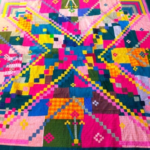 Puede incluir: Una colcha de retazos colorida con un diseño geométrico. La colcha está hecha de cuadrados y rectángulos en varios tonos de rosa, azul, verde, amarillo y naranja.