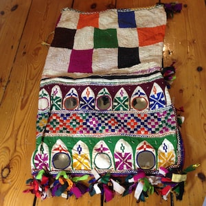 以下が含まれることがあります： 幾何学模様のカラフルなパッチワーク生地。小さな丸い鏡が1列に並んだデザインで、フリンジの縁取りが施されています。生地は綿製で、刺繍とビーズで装飾されています。