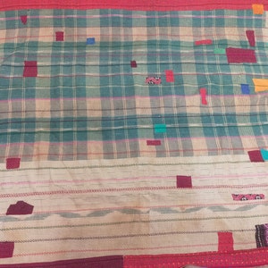 Op de afbeelding: Een geweven wandkleed met een ruitpatroon in tinten groen, bruin en roze. Het wandkleed is versierd met kleurrijke lappen stof in verschillende vormen en maten.