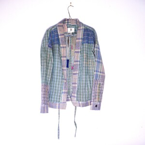 Puede incluir: Una chaqueta larga de manga larga con un patrón de patchwork a cuadros en tonos azules, verdes y rosas. La chaqueta tiene un cierre de corbata y una etiqueta que dice "B" en la parte delantera.