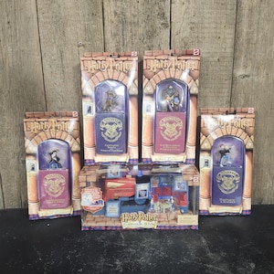 May include: A collection of five Harry Potter themed toy sets in original packaging. Four vertical boxes feature character figurines atop purple or red tins with Hogwarts crests. One horizontal box contains a Platform 9 3/4 train set.