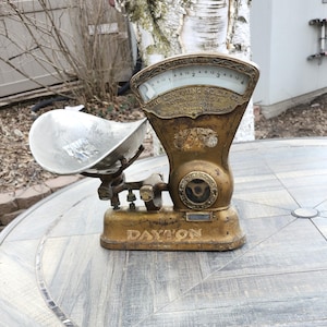 May include: Antique gold-colored scale with a silver pan. The scale has a circular face with black numbers and the text "The Computing Scale Co. Dayton, Ohio, U.S.A. Patented June 20, 1899." The scale also has the text "Dayton" on the base.