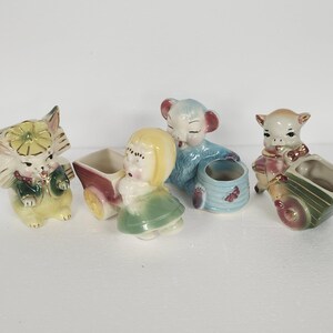 May include: A collection of vintage ceramic figurines. The figurines include a cat, a girl with a wagon, a koala bear, and a pig, each with a small planter. The figurines are painted in pastel colors with gold accents.