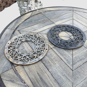 May include: Two decorative metal vent covers with intricate designs. One is painted white and the other is black.