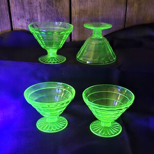 May include: Four vintage, bright green glass dessert dishes. Two are upright, with a bowl shape and a decorative base. One is upside down, and the other is a bowl shape. The glass has a ribbed design.