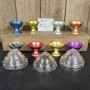 May include: A collection of colorful metal and glass serving dishes. The set includes small, pedestal-style bowls in blue, green, silver, and copper, along with clear glass serving dishes with lids. A handwritten note reads "Set #2".
