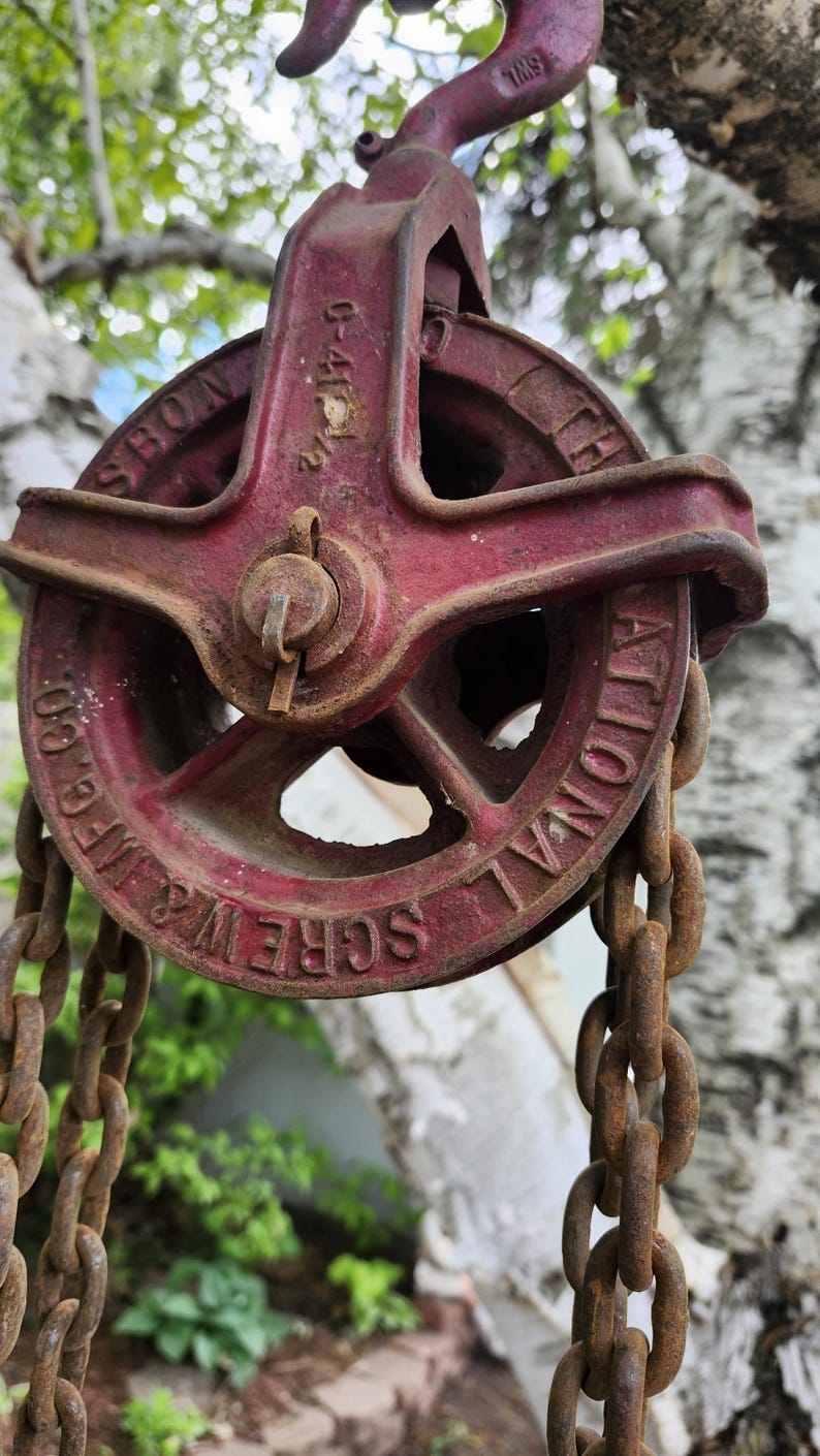 K&ouml;nnte beinhalten: Vintage rote Metallrolle mit Kette. Auf dem Rollenrad sind die Worte "NATIONAL SCREW & MFG CO" und "SBON" eingepr&auml;gt. Kette und Rolle weisen Rostspuren auf.