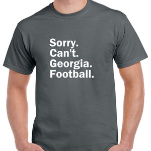 Puede incluir: Una camiseta gris oscuro con texto blanco que dice "Lo siento. No puedo. Georgia. F&uacute;tbol."