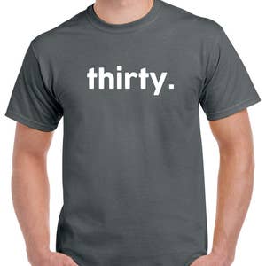 Puede incluir: Una camiseta gris oscuro con la palabra "thirty." impresa en blanco en la parte delantera.