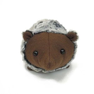 May include: A brown plush hedgehog with a gray and white fur trim. The hedgehog has black eyes and a small black nose.