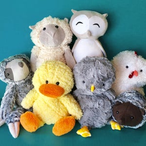 May include: A group of plush toys including a grey sloth, a yellow duck, a grey owl, a white sheep, a grey chicken, and a brown hedgehog.