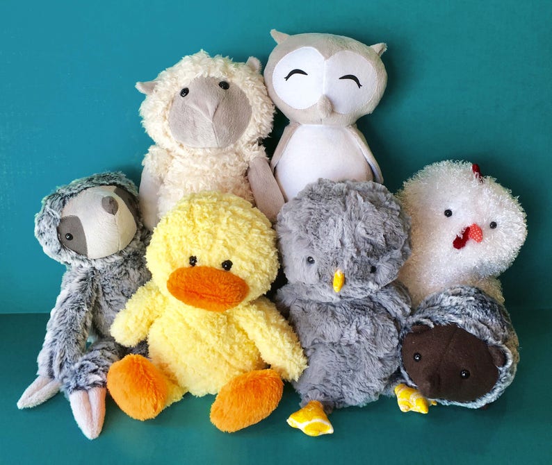 May include: A group of plush toys including a grey sloth, a yellow duck, a grey owl, a white sheep, a grey chicken, and a brown hedgehog.