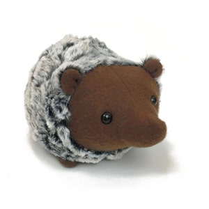May include: A brown and gray plush hedgehog toy with black eyes. The hedgehog has a soft, furry body and a cute, rounded face.